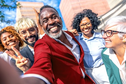 Mennesker av ulik alder, rase og kjønn smiler bredt utenfor en bygning