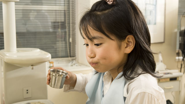 A girl sitting in a dental chair during an appointment, smiling nervously.